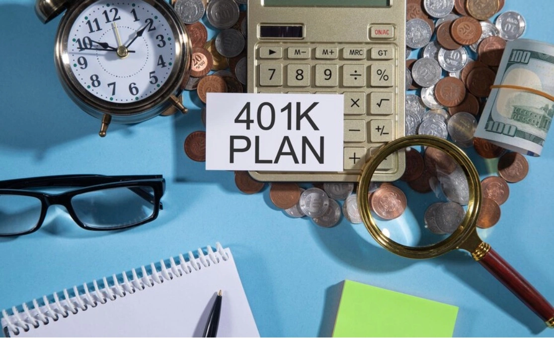 Notecard with '401K plan' written on it, calculator over coins, a wad of bills, a magnifying glass, glasses and a notebook