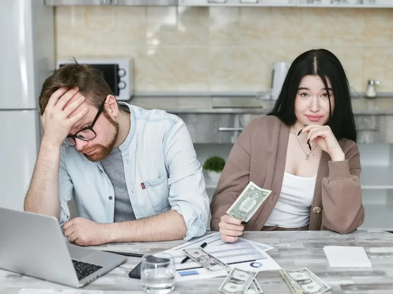 Couple doing taxes, man holding head in stress, woman holding a dolar