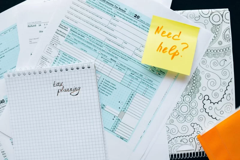 Taxing forms, a stickie with a 'Need help?' note and a notepad with 'tax planning' written.