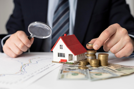 Salesman holding a magnifying glass and stackin coins with a miniature house